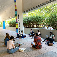 A group of students seated on the sidewalk outside the Neuberger Museum of Art