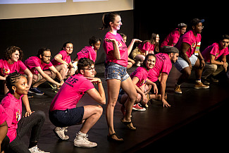 Photo of Orientation leaders wearing pink shirts dancing on stage with one standing up in the middle
