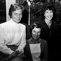 Archival black and white image of three women in seated positions facing the camera and smiling