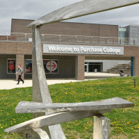 Person walks in distance with Welcome to Purchase College sign on brick building