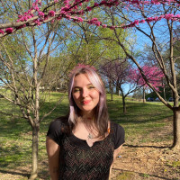 Student Lilliam Cheever smiling with her arms crossed behind her in from of a blooming tree with pink flowers