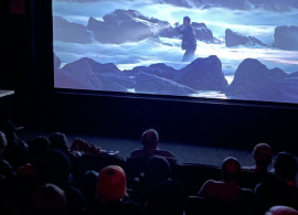 Photo of darkened cinema with blueish image of figure at seaside