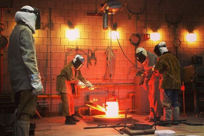 Students dressed in protective gear, forging metal in a metal foundry on campus.