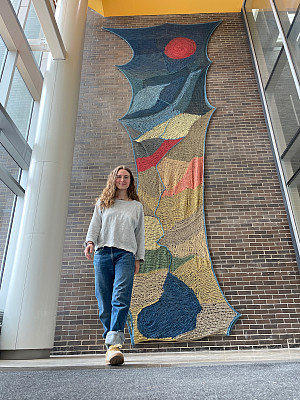 Rowan Perkins with her tapestry, A River to the Sky, in the Center for Media, Film, and Theater