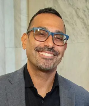 Man wearing glasses and a suit jacket smiling