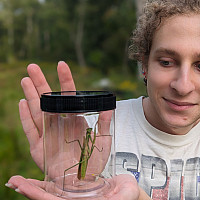 Student holds a container with a grasshopper.