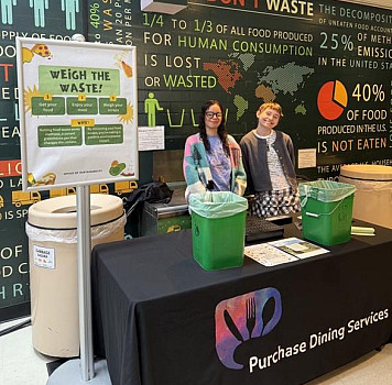 Two interns hosting Weigh the Waste event in the Dining Hall by compost station