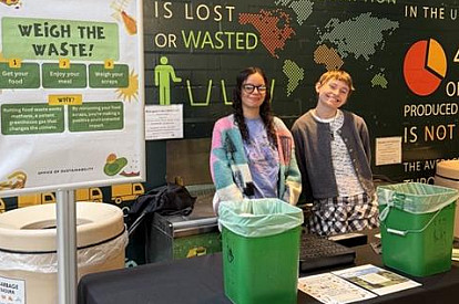 Two interns hosting Weigh the Waste event in the Dining Hall by compost station