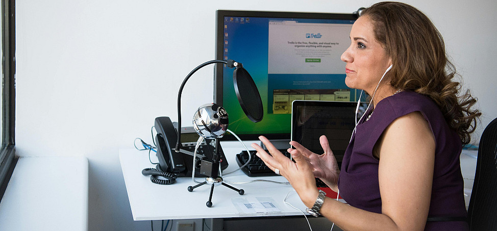 Woman at desk with mic and computer set up to podcast