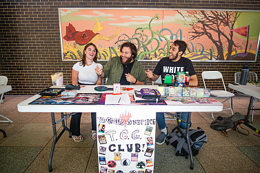 Three people smiling and laughing at a table outside of a building.