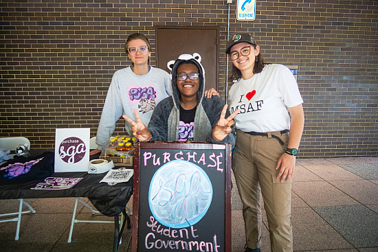 Three people smiling at a table outside of a building, with a PSGA sign.