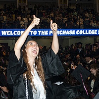 Student in black grad cap and gown looks up and give two thumbs up