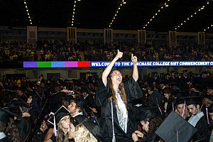 Student in black grad cap and gown looks up and give two thumbs up