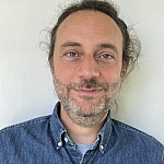 Photo of a man with facial hair and a blue collared shirt