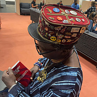 Photo of the artist Romuald Hazoumè wearing a hat covered with pins