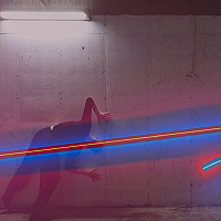 Colorful neon artwork hangs on a wall, a dancer poses in front of it