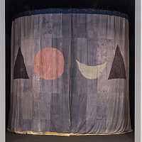A fabric curtain with a geometric design hangs in a doorway, featuring a large red circle, a smaller white crescent, and two black triangles