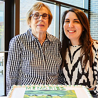 Two smiling women pose with a cake.