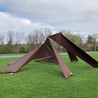 Photograph of a unique, perspective-warping abstract steel metal sculpture set on a green lawn.