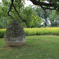 Large gray egg-shaped stone sculpture in a field.