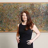 woman in a black dress with her hands on her hips stands in front of a large abstract painting
