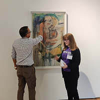 de Kooning's Marilyn Monroe painting in a white frame on gallery wall, a man and a woman stand in front of it.
