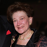 Four adults dressed in formal evening attire stand together and smile at the camera at a social or gala event, with a blurred background.