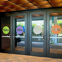 Photo of the entrance to the Museum featuring four glass doors, each with a decal of the letters neu centered in a color circle.