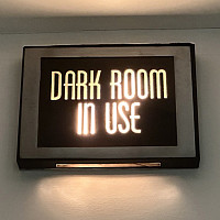 A lit wall sign with the words DARK ROOM IN USE in bold, illuminated letters, indicating that the dark room is currently occupied.