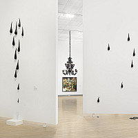 Contemporary art gallery with white walls, featuring black teardrop-shaped sculptures mounted at varying heights and a black chandelier in t