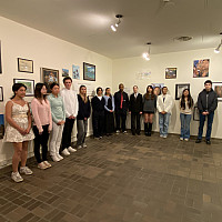 A group of high school students pose for a photo in an art gallery with artwork on the wall behind them.
