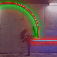 An artwork made up of colorful neon tubes on a wall with a dancer posing in front of it
