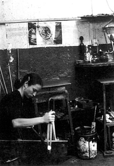 Black and white archival image of artist Rosalie D. Gagné in her studio with a Mexican flag on the wall and with a compass in her hands.