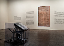 Museum gallery with a large case in the foreground and wall text and an image of the declaration of independence in the background