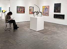 Image of a college-age student seated on a stool with a sketchpad drawing works from the Museum's collection