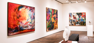 A modern art gallery with brightly colored abstract paintings on white walls, spotlights above, and two white sculptures displayed on black
