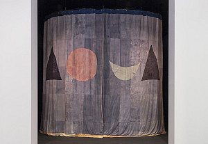A fabric curtain with a geometric design hangs in a doorway, featuring a large red circle, a smaller white crescent, and two black triangles
