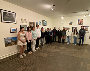 A group of high school students pose for a photo in an art gallery with artwork on the wall behind them.
