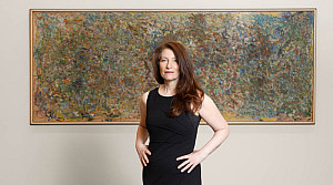 woman in a black dress with her hands on her hips stands in front of a large abstract painting