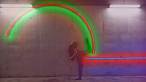 An artwork made up of colorful neon tubes on a wall with a dancer posing in front of it