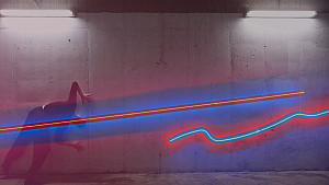 Colorful neon artwork hangs on a wall, a dancer poses in front of it