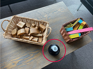 Magic 8 Ball with a red circle on a table with baskets of wooden blocks
