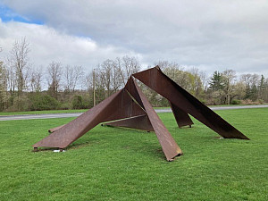 Photograph of a unique, perspective-warping abstract steel metal sculpture set on a green lawn.