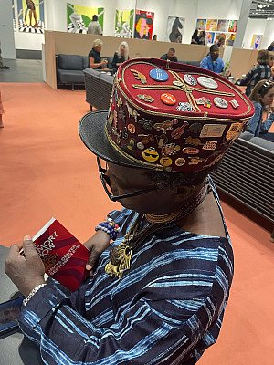 Photo of the artist Romuald Hazoumè wearing a hat covered with pins
