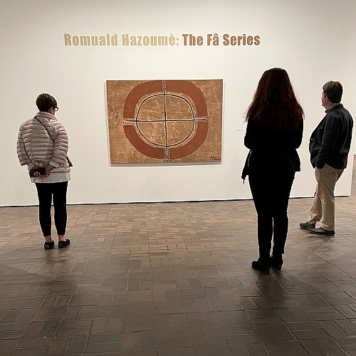 A view from behind two women and one man in a gallery looking at an artwork from the Romuald Hazoume exhibition