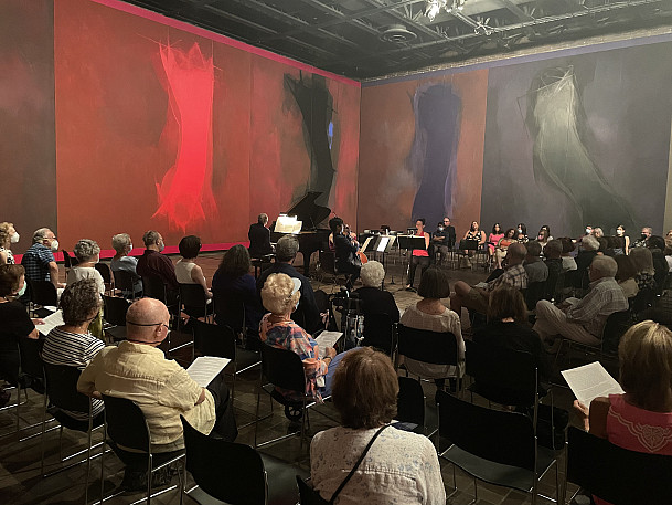 Photo of musicians surrounded by an audience and the Threnody painting