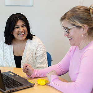 Smiling student and smiling instructor with laptop.