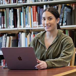 Smiling student in front of laptop in library.