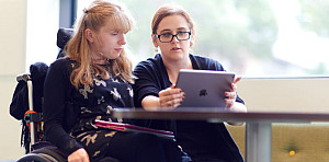 Girl in a wheelchair talking with her Professor about what is on their iPad screen