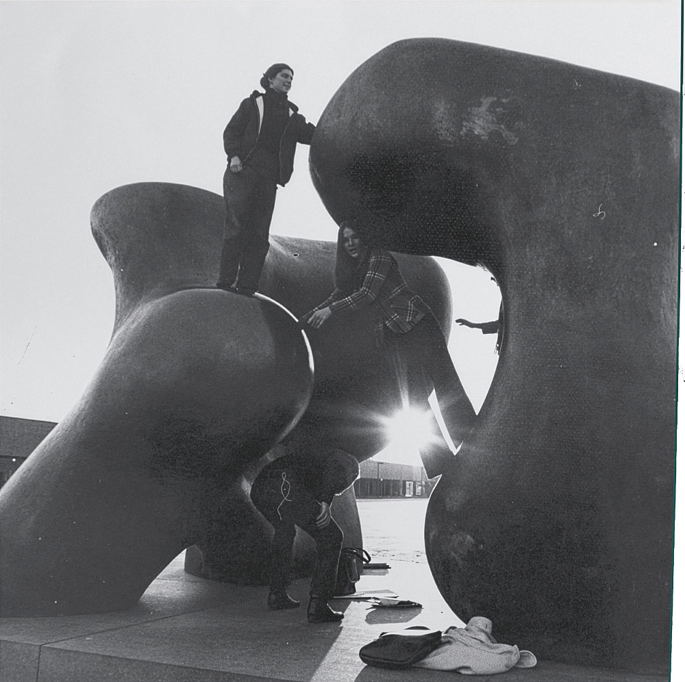 Students climb on Henry Moore's Large Two Forms sculpture with sun setting